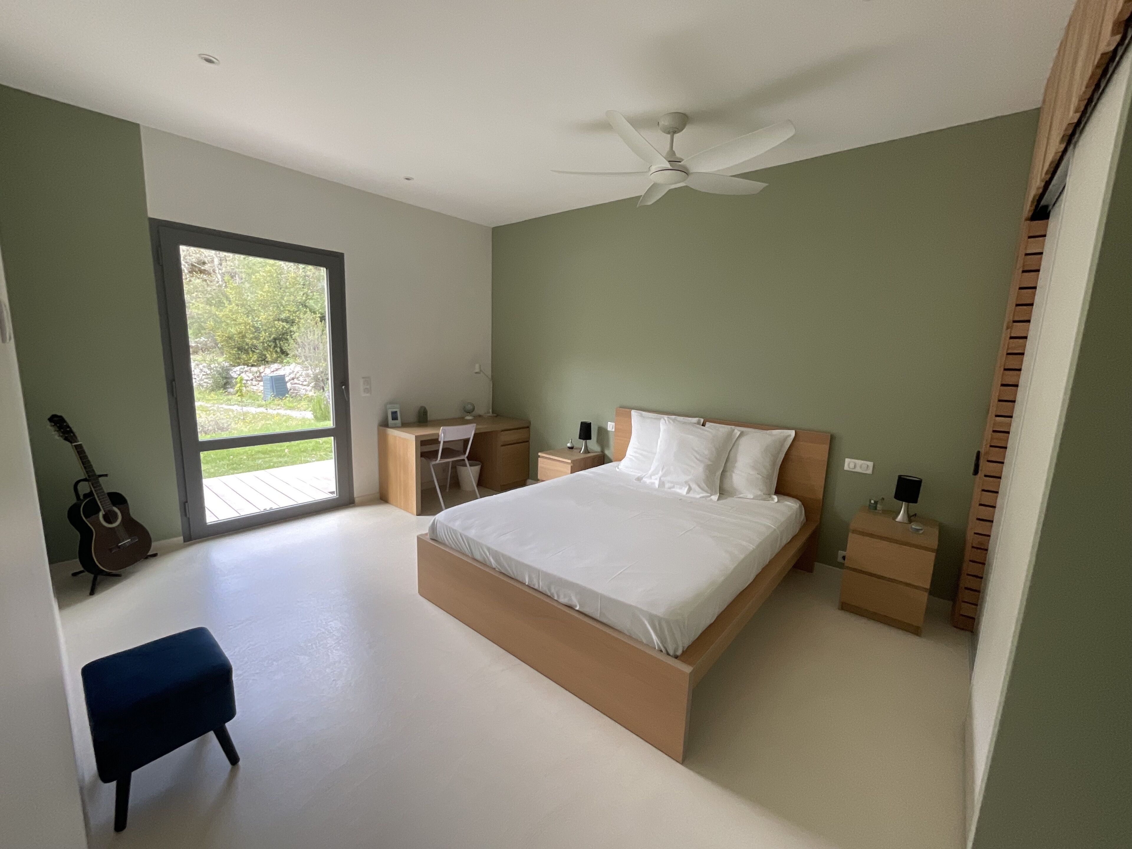 Ein Schlafzimmer mit Bett, Schreibtisch, Stuhl, Gitarre und Deckenventilator.