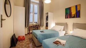 Ein Hotelzimmer mit zwei Betten, einem Schreibtisch mit Stuhl, einem Spiegel und einem Bild an der Wand.