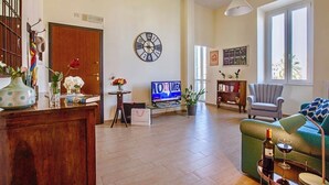 Ein Wohnzimmer mit Fernseher, einer Uhr, einem Sofa, einem Sessel und einem Fenster.