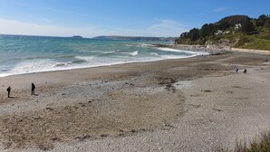Une plage avec un rivage rocheux, des gens qui se promènent et un ciel dégagé.