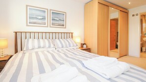 Une chambre d’hôtel avec un lit, deux tableaux encadrés au mur, une table de chevet avec une lampe et une armoire en bois.