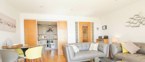 A modern living room with a grey sofa, a glass coffee table, and a dining area with a yellow chair.