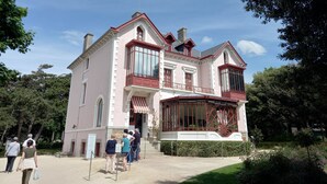 Un bâtiment historique à la façade rose, doté de grandes fenêtres et d’un balcon imposant.