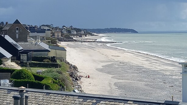 Une vue sur la côte, avec une plage, des maisons et une colline au loin.