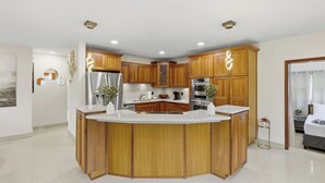 A modern kitchen with wooden cabinets, a central island, stainless steel appliances, and recessed ceiling lights. - Miami Tropical Retreat: Private Pool & Patio (Miami)