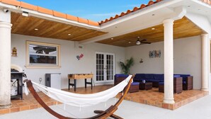 Un hamac sous une pergola en bois, un espace patio avec un canapé bleu et un sol carrelé.