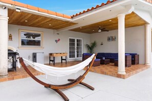 Una hamaca bajo una pérgola de madera, un área de patio con un sofá azul y un piso de baldosas.