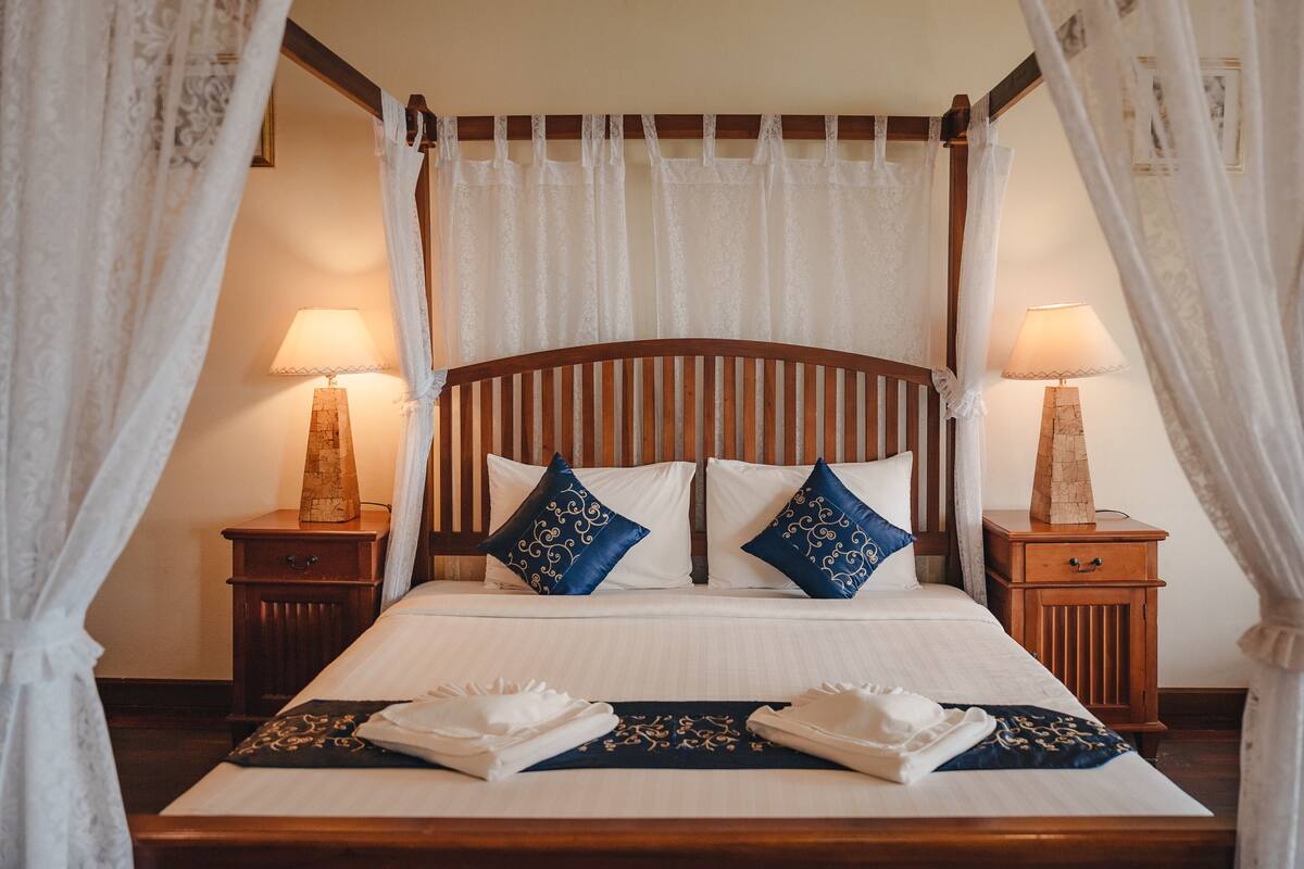 A neatly made bed with white linens and blue decorative pillows, flanked by wooden nightstands with lamps.