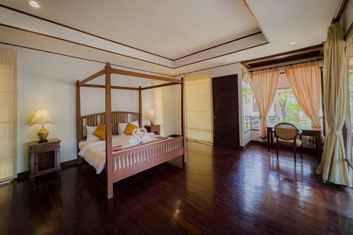 A four-poster bed with a wooden frame, a nightstand with a lamp, and a chair by the window.