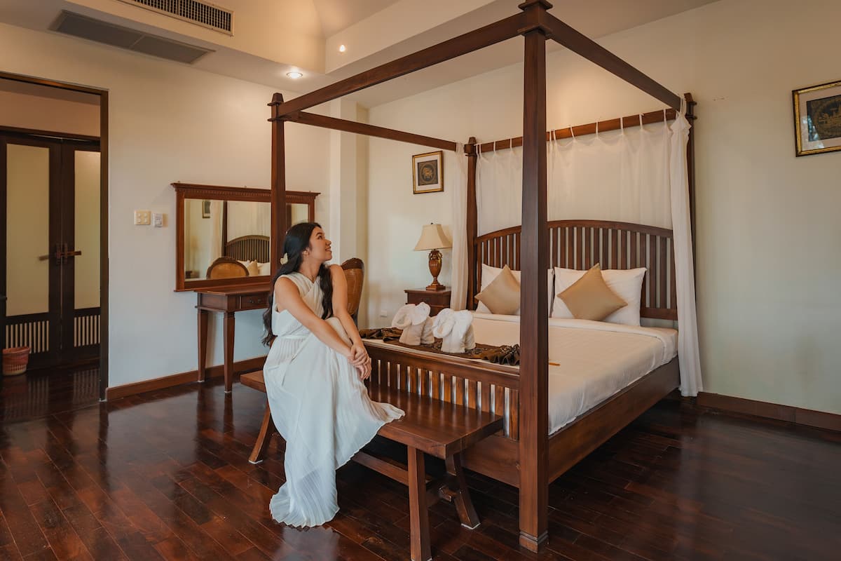 A four-poster bed with a canopy, a wooden nightstand, a mirror, and a lamp.