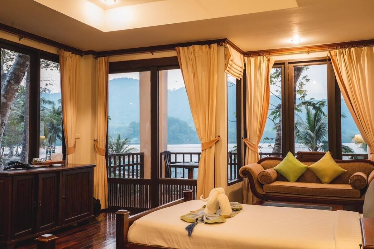 A hotel room with a bed, a sofa, and a view of the beach and mountains.
