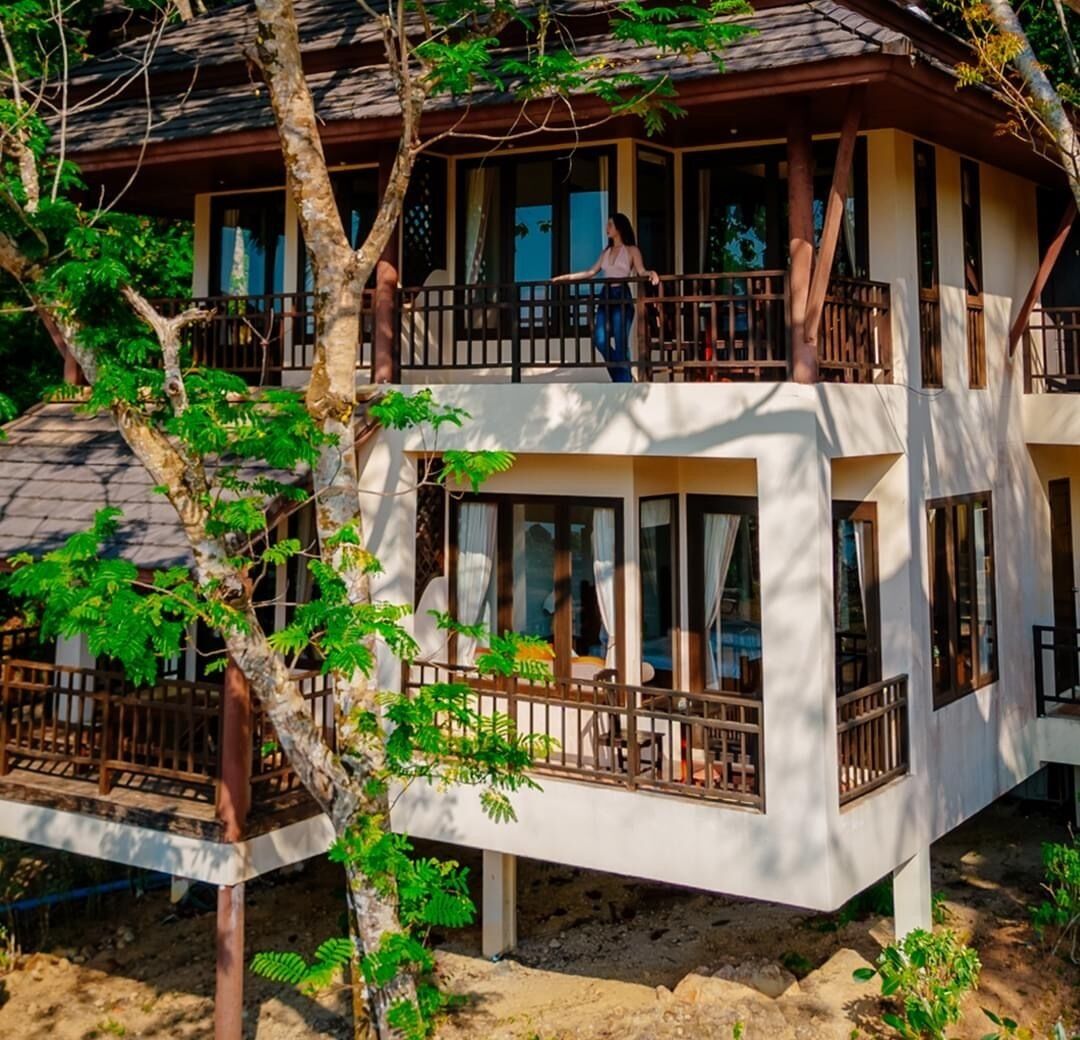 Un immeuble à deux étages doté de balcons, de grandes fenêtres et d’un arbre au premier plan.