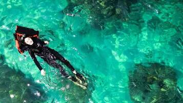 Eine Person schwimmt in klarem türkisblauem Wasser vor steinigen Felsen.