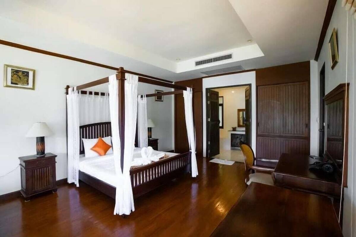 A four-poster bed with white bedding, a wooden nightstand with a lamp, and a wooden dining table with chairs.