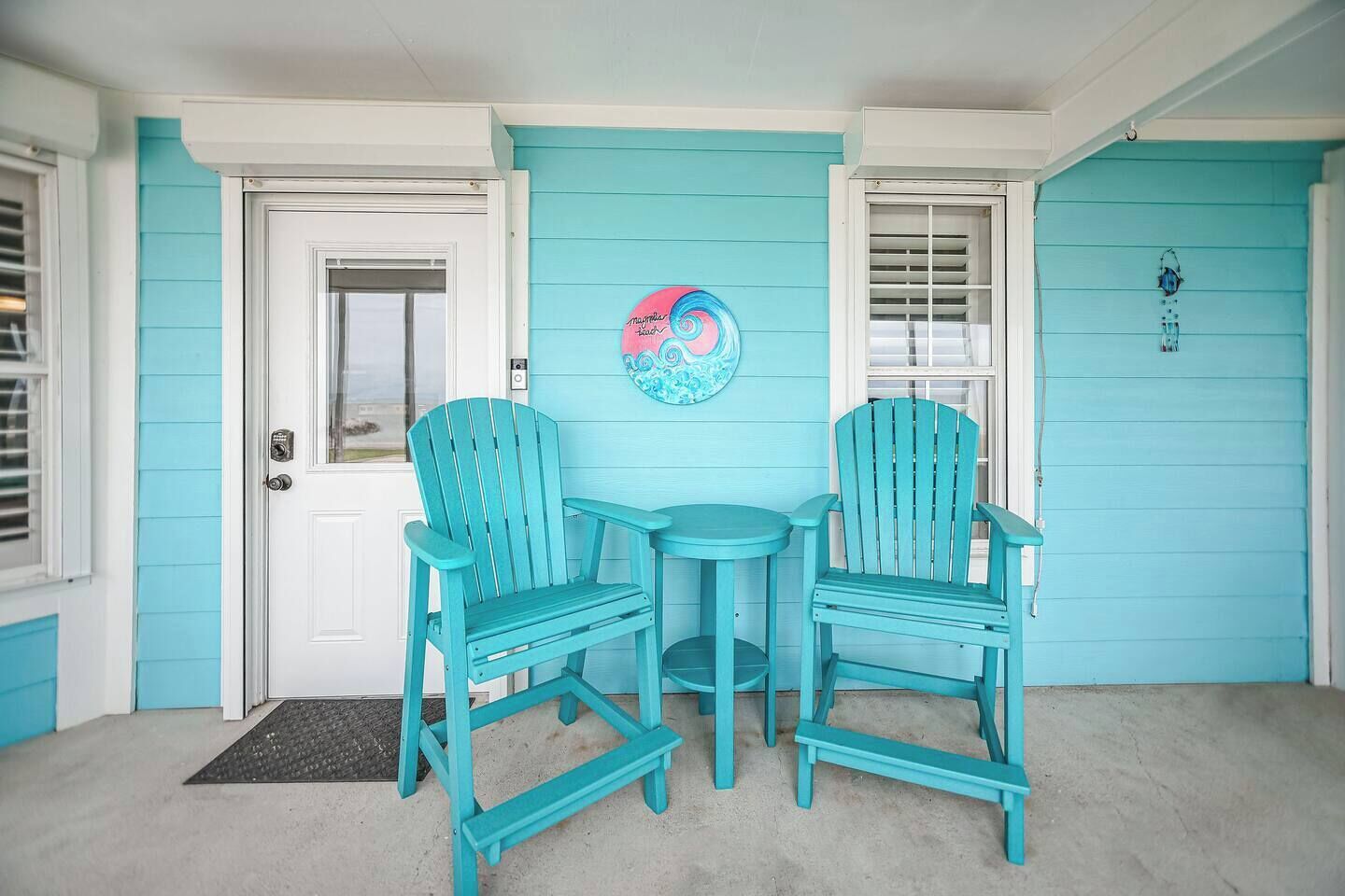 Une véranda avec deux fauteuils Adirondack turquoise et une petite table ronde.