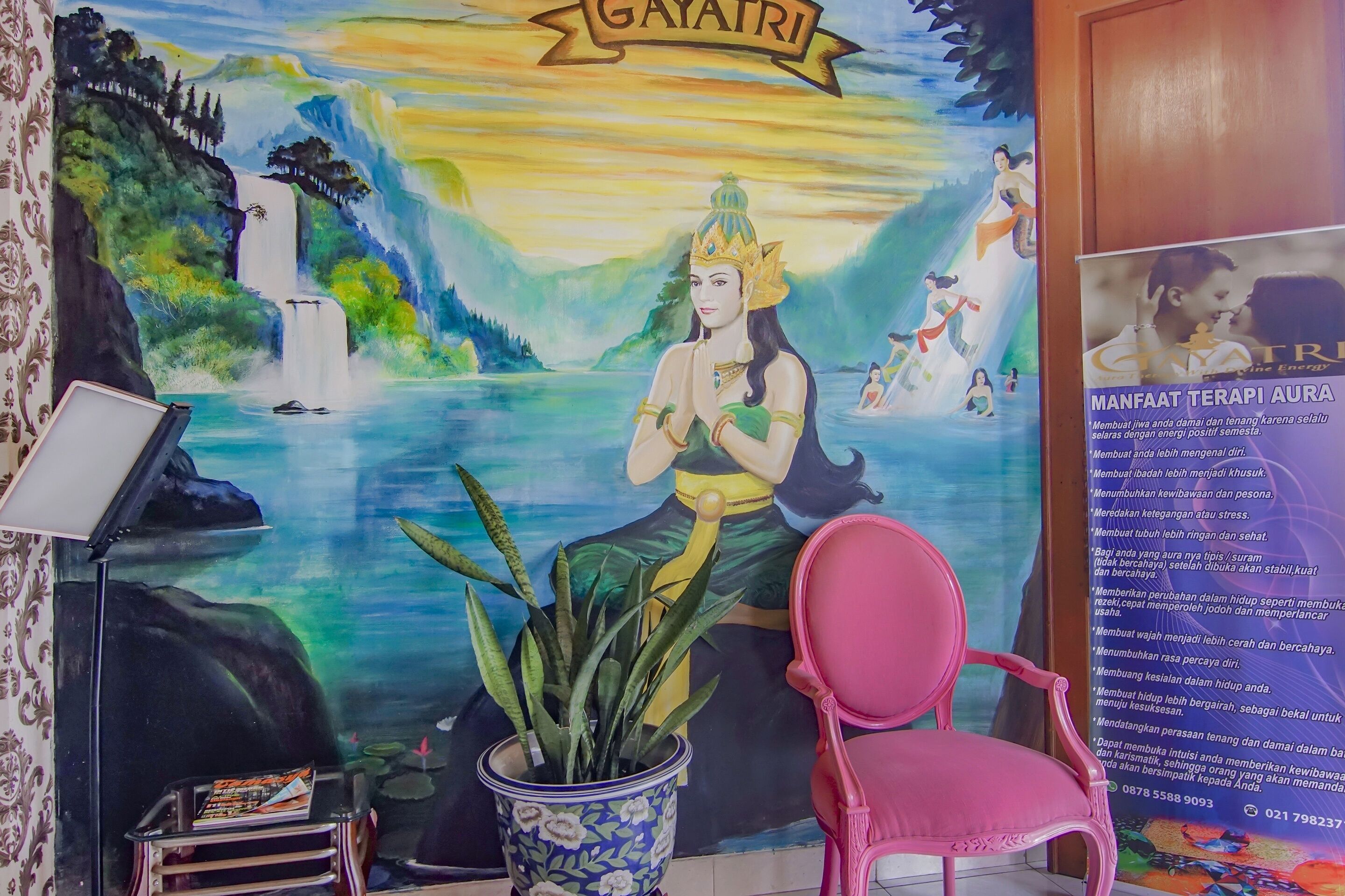 A room with a mural of a waterfall and a figure, a potted plant, a pink chair, and a poster on the wall.