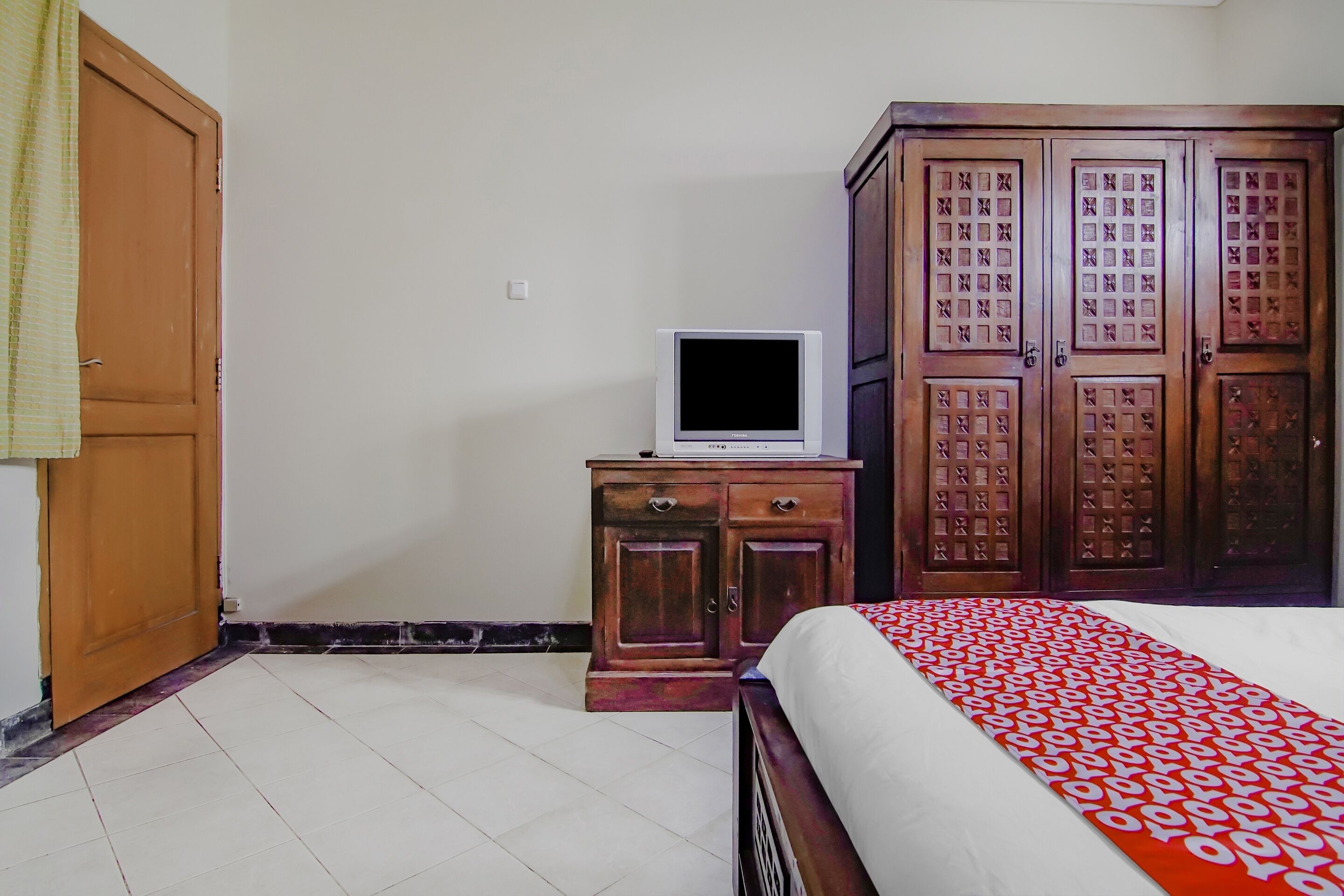 A bedroom with a bed, a wooden wardrobe, a small cabinet with a television on top, and a partially open door.