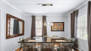Une salle à manger avec une table rectangulaire, six chaises, un grand miroir, un tableau coloré et un tapis à motifs.