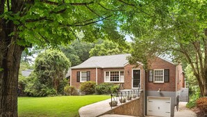 Une maison à deux étages, construite en briques, avec un jardin devant, un garage et un escalier menant à l’entrée.