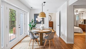 Un espace repas moderne avec une table ronde en bois, des chaises à revêtement gris et un luminaire suspendu en fibres tressées.