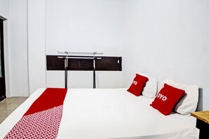 Habitación de hotel con una cama, una alfombra roja y blanca estampada, y dos almohadas rojas con la palabra 'YOYO' escrita en ellas.