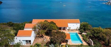 Una propiedad costera con piscina, edificios blancos y vistas al mar y las montañas.