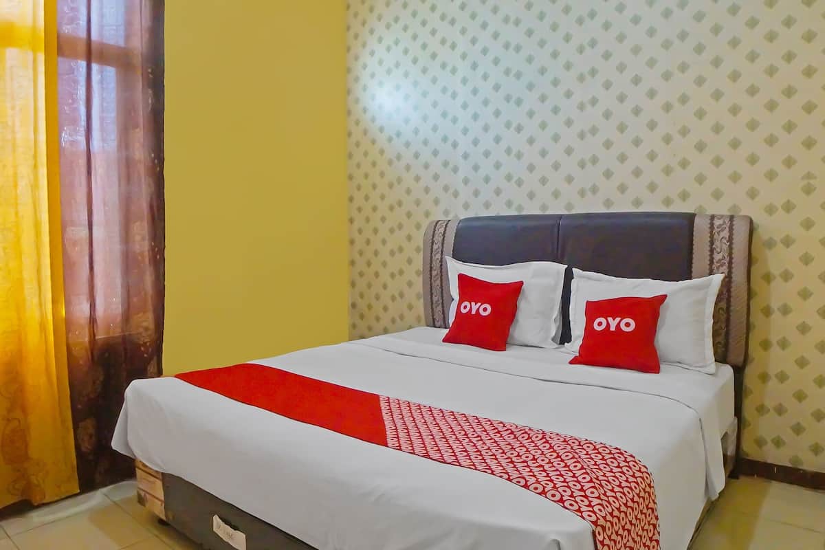 Hotellihuone, jossa on sänky, kaksi punaista koristetyynyä, joissa on «OYO»-merkki, kuvioitu punavalkoinen peitto ja kuvioitu seinä.