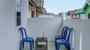 Ein schmales Außenareal mit einem Tisch und zwei blauen Plastikstühlen, auf dem Tisch ein Laptop, und eine weiße Wand.
