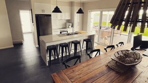 A modern kitchen with a central island, black bar stools, and pendant lighting.
