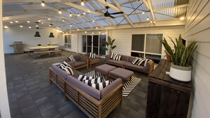 An outdoor patio with a covered seating area, string lights, and a grill.