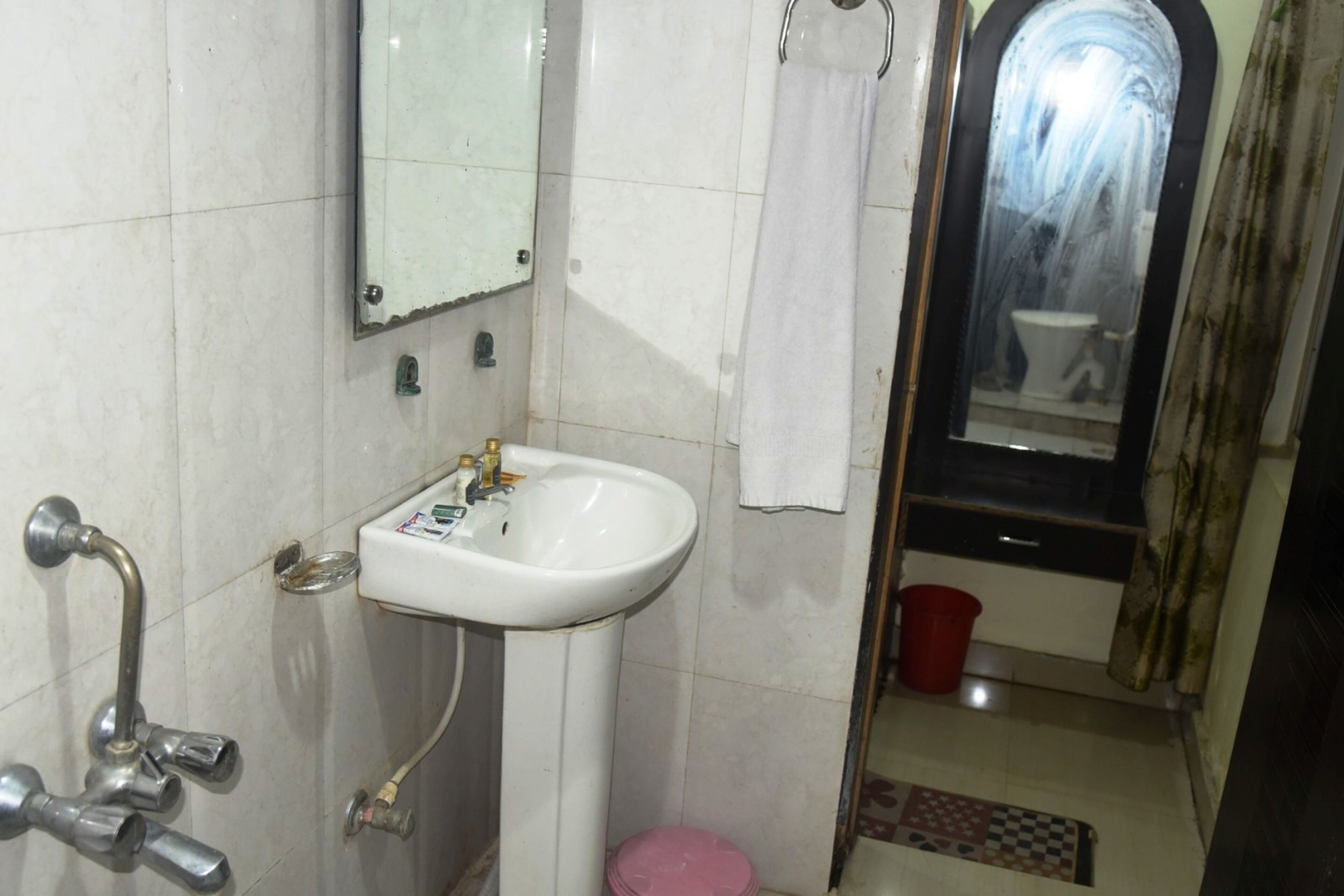 Une salle de bain avec un lavabo blanc, un miroir, une douche et un seau rouge.