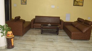 A living room with a brown leather sofa, a wooden coffee table, and a potted plant. - Hotel Udika Palace (Singrauli)