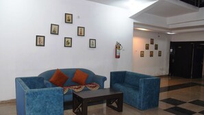 A lobby with two blue sofas, a coffee table, and framed pictures on the walls. - Hotel Udika Palace (Singrauli)