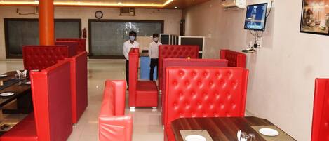 A restaurant with red upholstered booths and a wooden dining table with white placemats and cutlery.