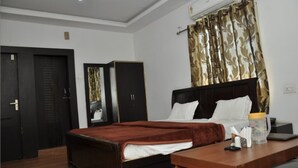A hotel room with a bed, a desk, a wardrobe, and a curtain. - Hotel Udika Palace (Singrauli)