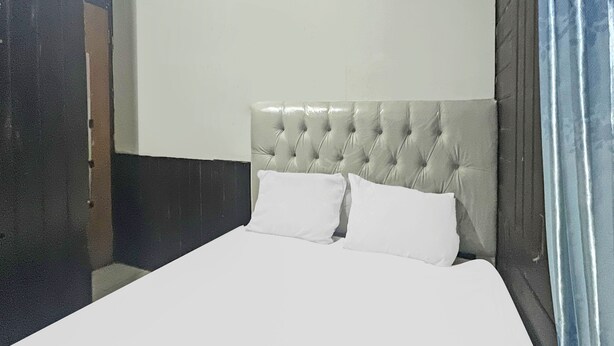 Een bed met een gestoffeerd hoofdbord, twee witte kussens en een effen witte muur.