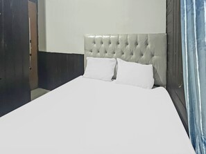 A bed with a tufted headboard, two white pillows, and a plain white wall. - SPOT ON 91793 Maila Homestay  (Tenggarong)