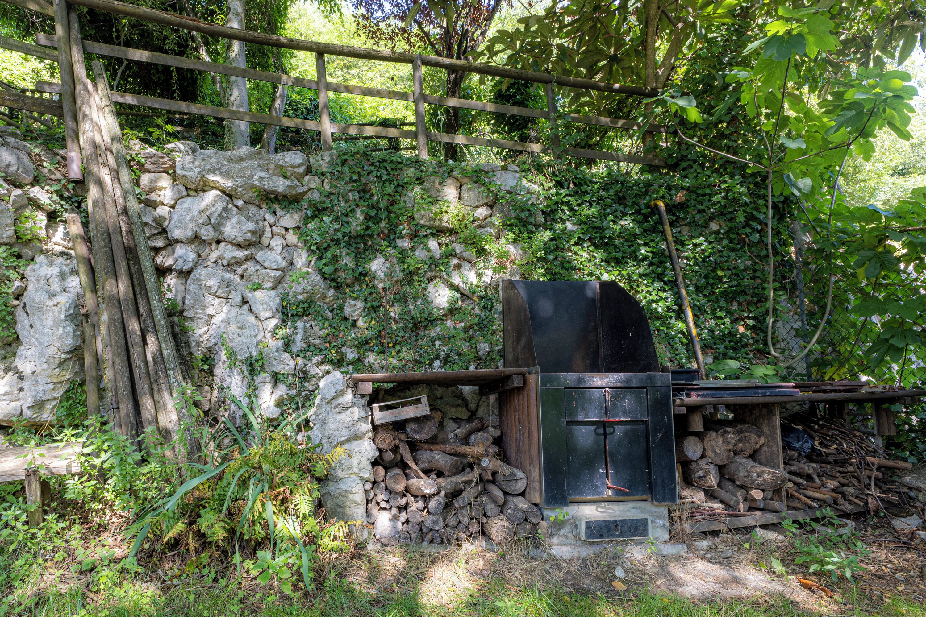 Un espacio rústico para cocinar al aire libre, con pared de piedra, troncos de madera y una parrilla de metal.