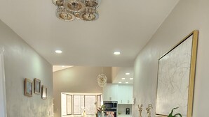 A spacious hallway with a wooden floor, a central island with seating, a kitchen area in the background, and a large framed artwork on the wall. - Beautiful and cozy home in a safe and private environment (Alajuela)