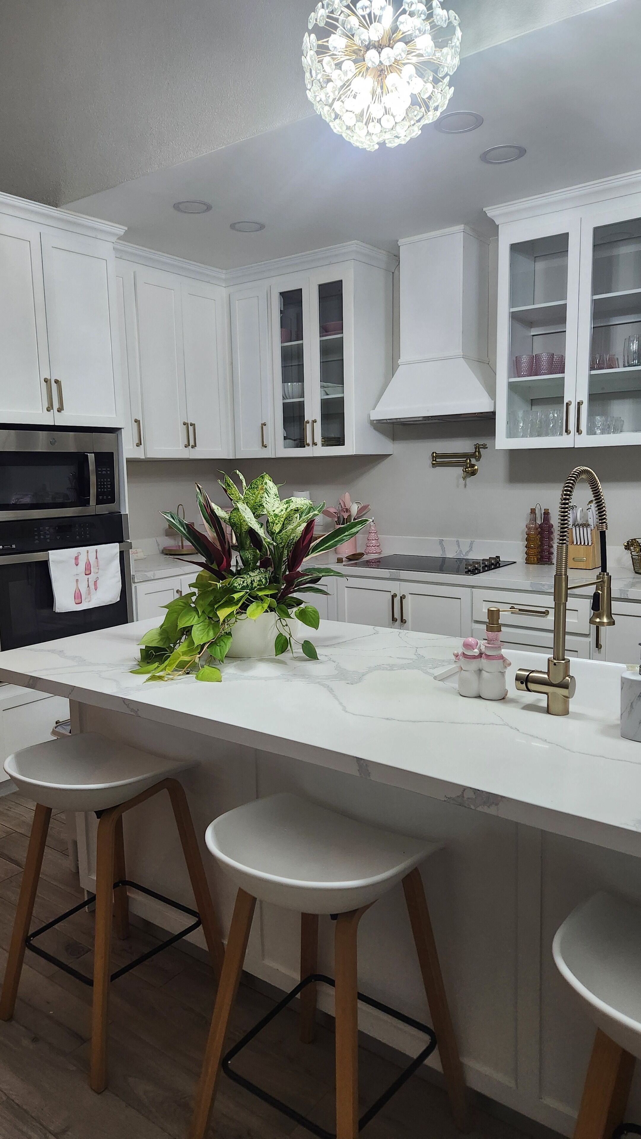 A modern kitchen with white cabinets, a central island with stools, a chandelier, and a stainless steel oven.