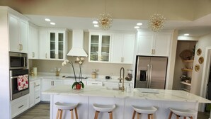 A modern kitchen with white cabinetry, stainless steel appliances, and a marble island with bar stools. - Beautiful and cozy home in a safe and private environment (Alajuela)