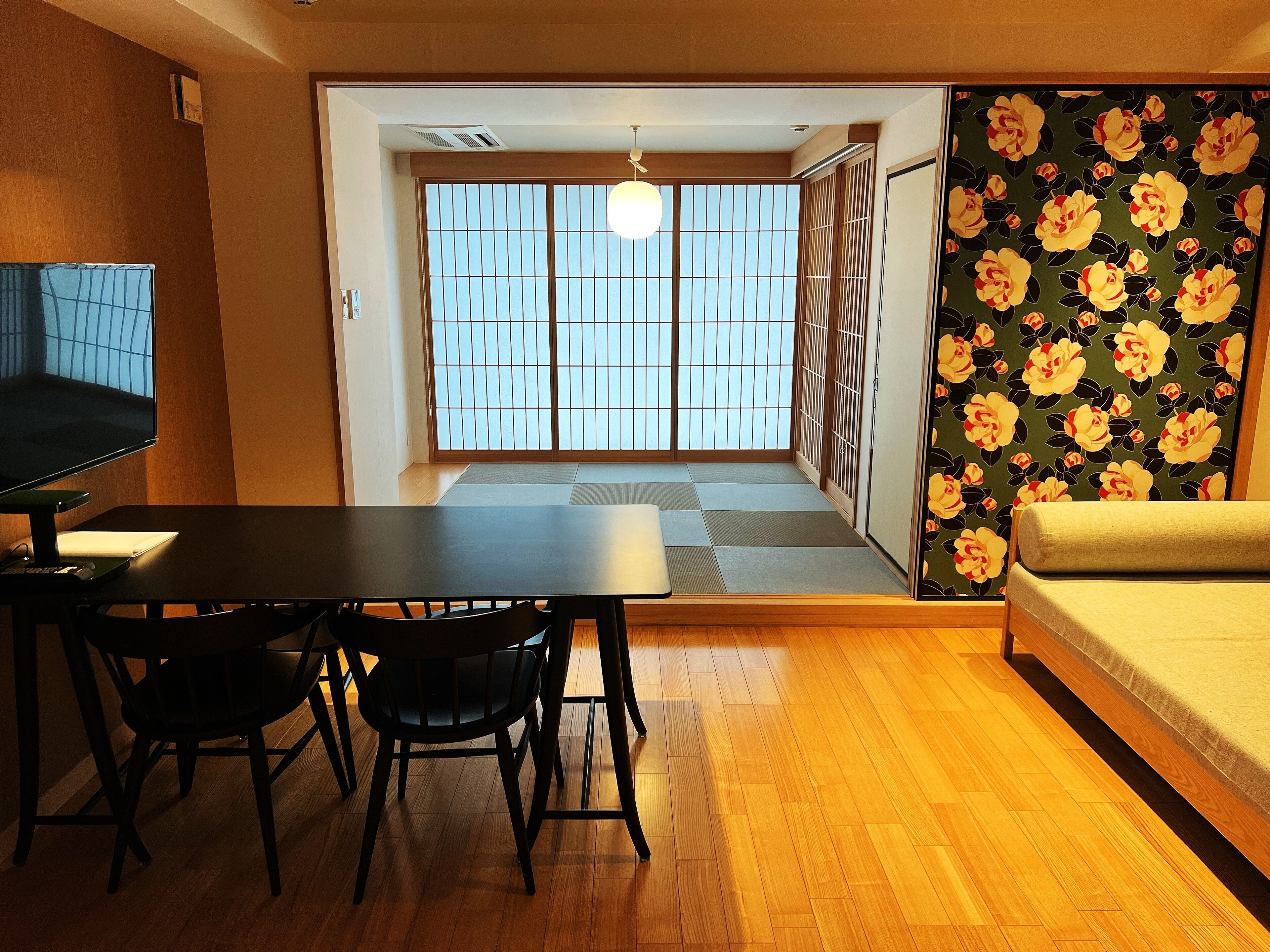 A traditional Japanese room with tatami flooring, a low table with chairs, a sofa, and a sliding door with a floral wallpaper.