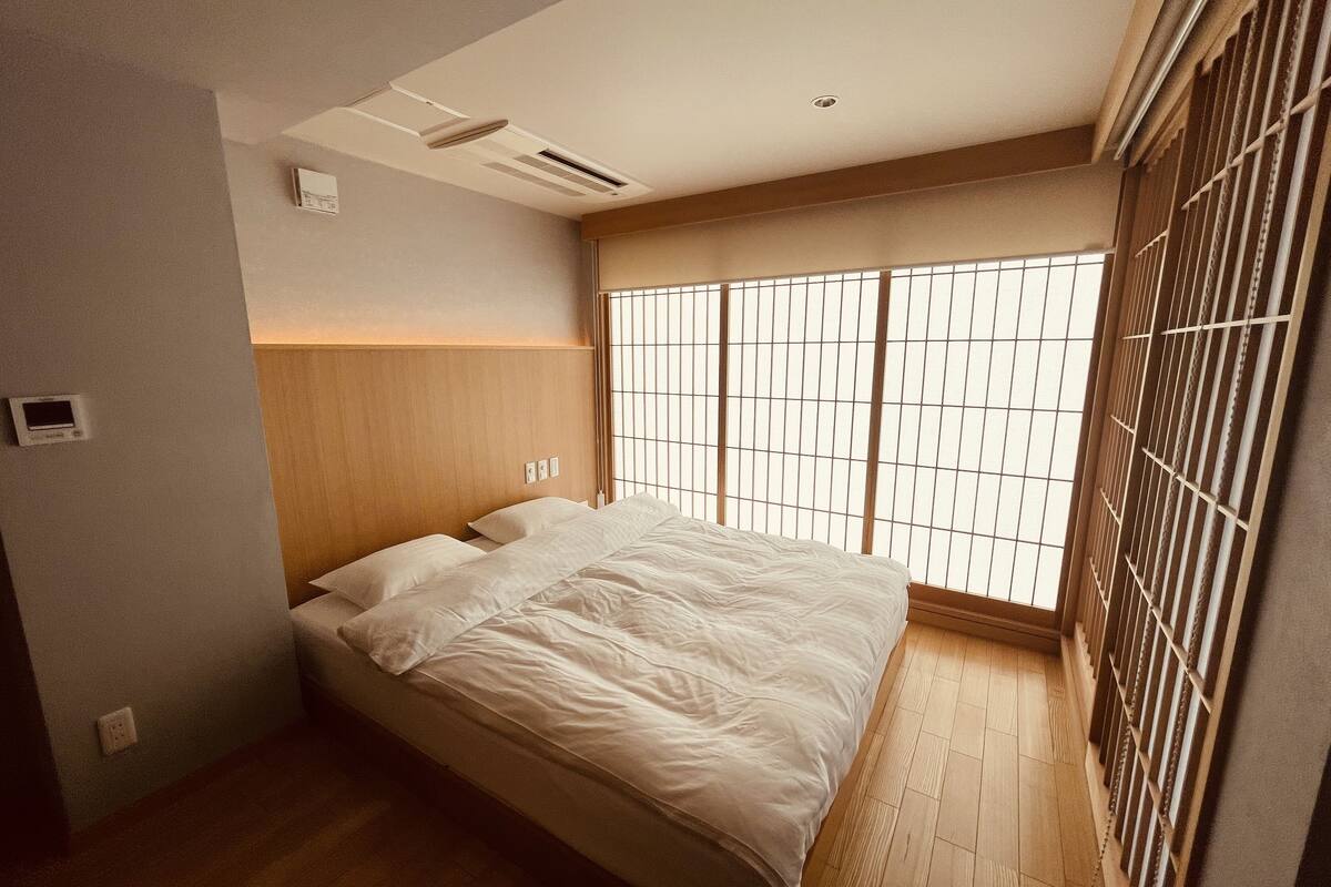 Un dormitorio con cama, cabecera de madera y ventana con celosías japonesas.