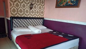 A bed with a patterned headboard, a red blanket, and a wall with a floral wallpaper and a framed picture. - OYO Life 3020 Penginapan Citra Rasa (Plaosan)