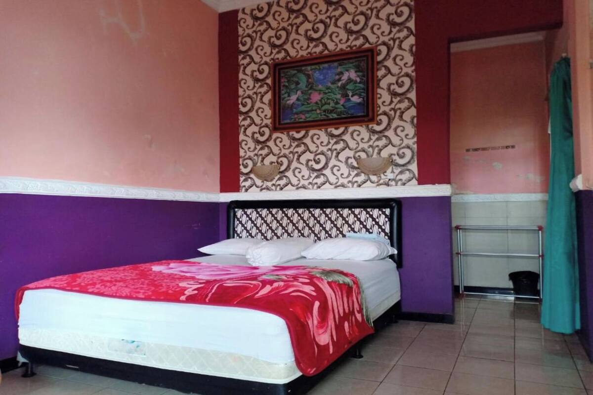Ein Bett mit einer rot-weißen Tagesdecke, einem gemusterten Kopfteil und einer Wand mit einem floralen Gemälde.
