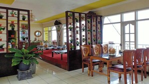 A spacious room with a tiled floor, a wooden dining table with chairs, a red carpet, and a large window providing natural light. - OYO Life 3020 Penginapan Citra Rasa (Plaosan)