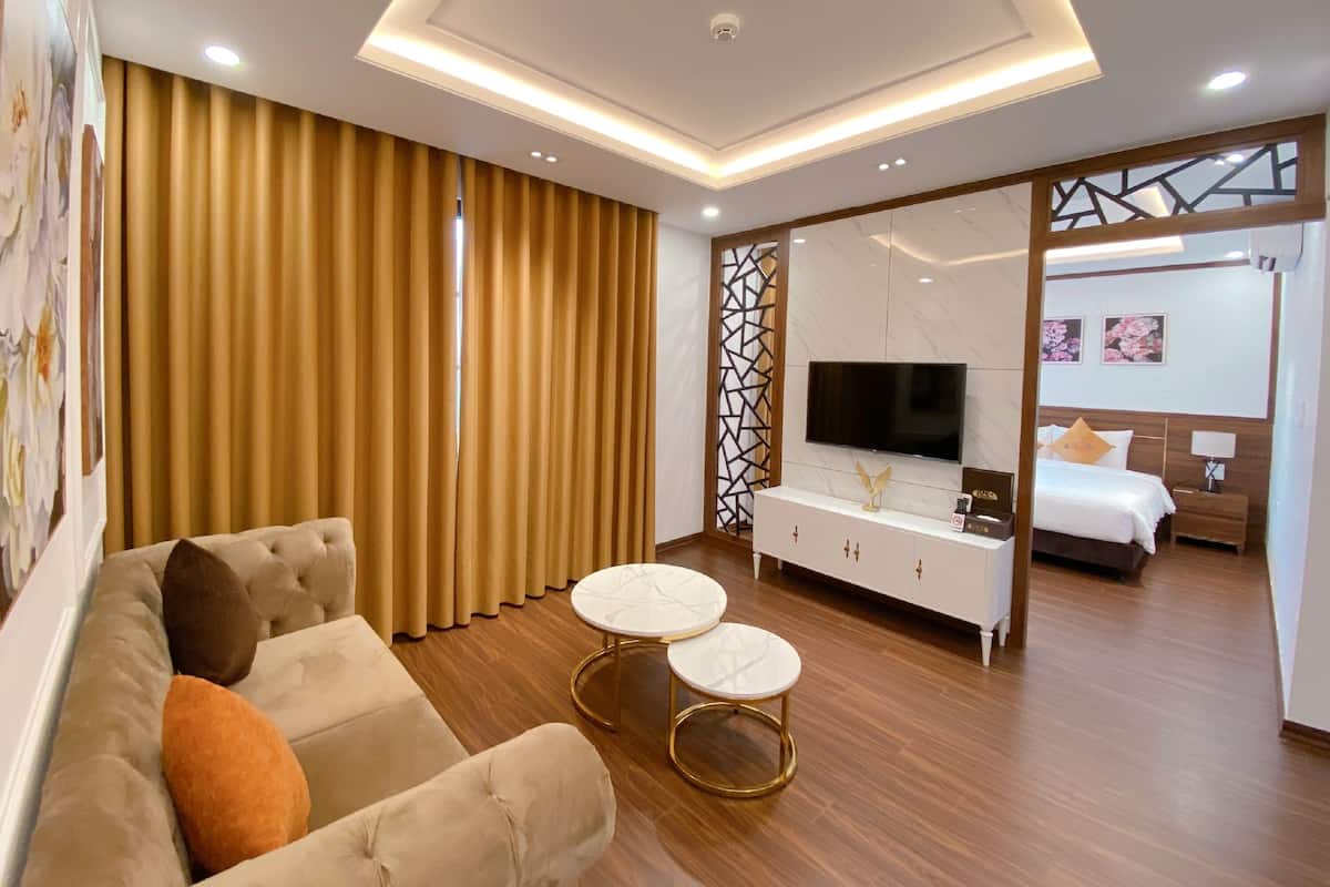 A modern hotel room with a sofa, two round tables, a TV, a bed, and a sliding door leading to another room.