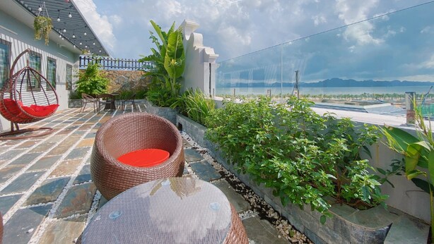 A rooftop terrace with wicker furniture, a stone wall, and a view of the sea. - JADE HA LONG HOTEL (Bai Chay)