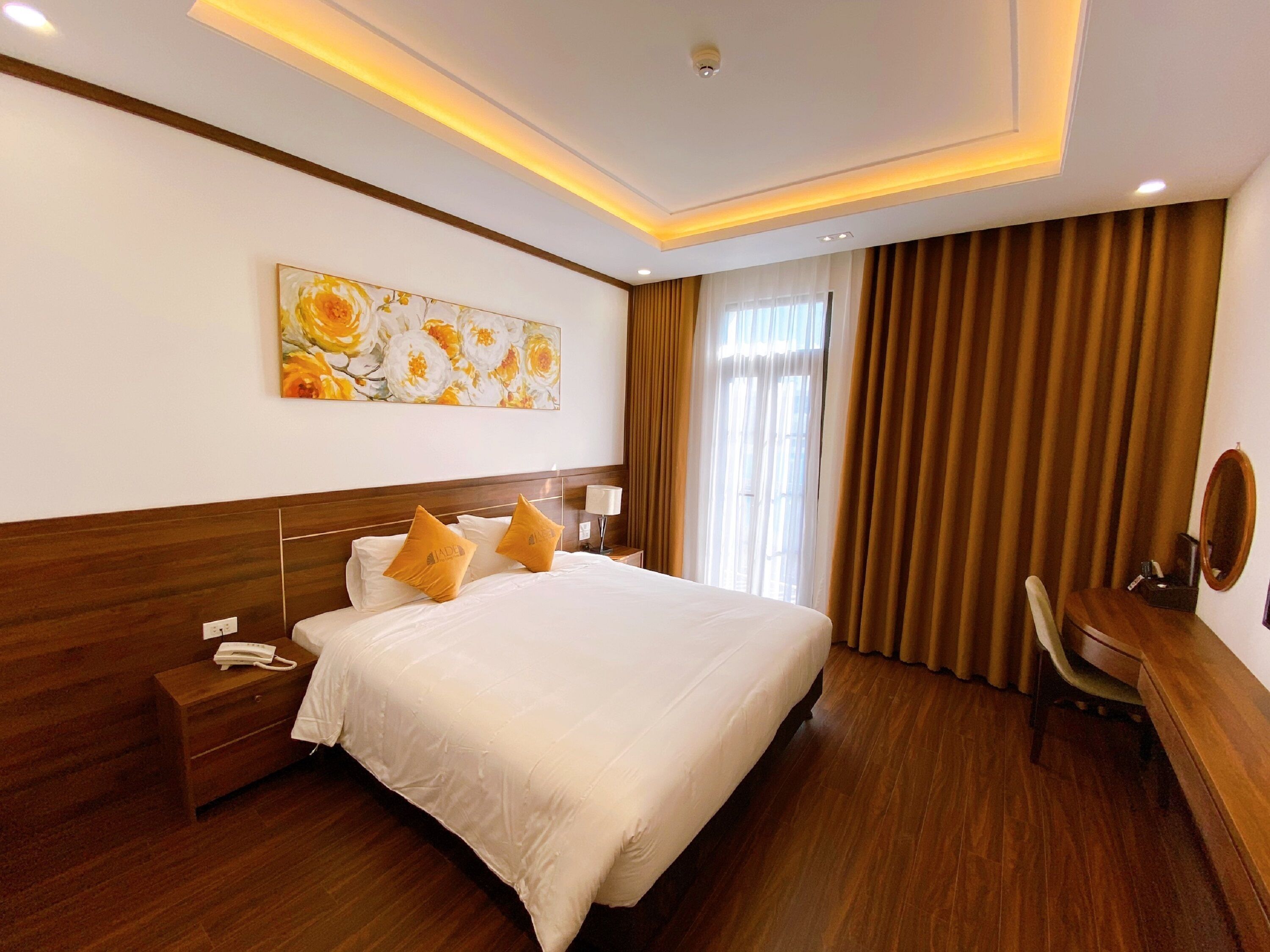 A hotel room with a large bed, wooden headboard, a desk with a chair, a telephone, and a painting on the wall.