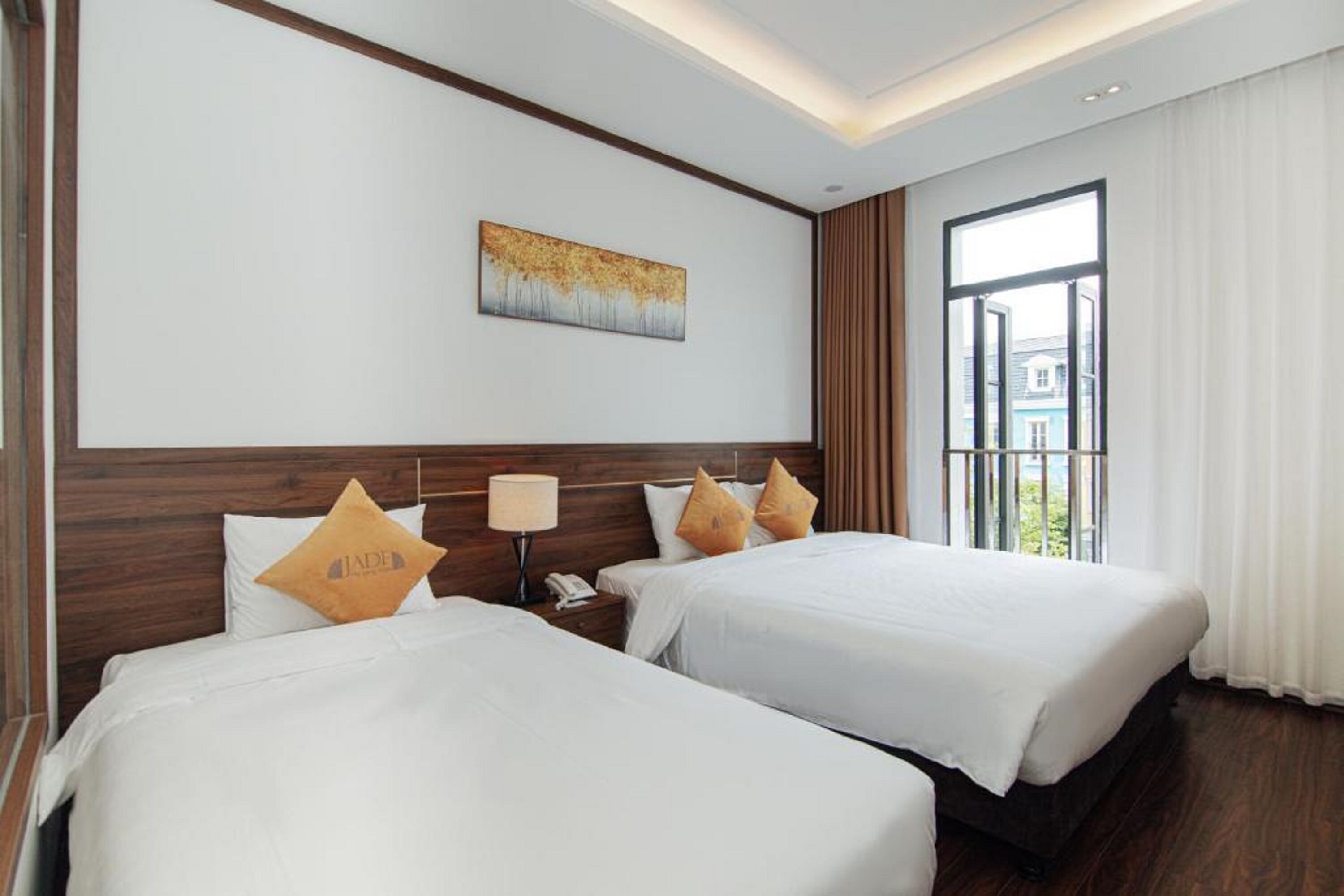 Habitación de hotel con dos camas, una mesita de noche, una lámpara, un cuadro en la pared y un ventanal con cortinas.